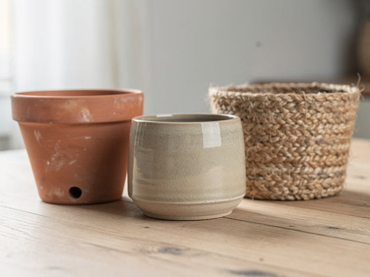A terracotta pot, a glazed ceramic planter, and a woven basket planter grouped together on a table