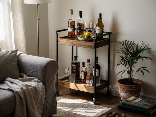 A small bar cart with a few bottles and glasses set up in the corner of a compact apartment