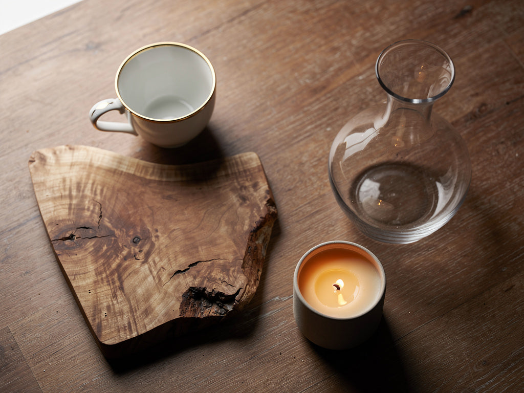 A flat lay of hostess gift options including a decanter, a small coffee cup, a candle, and a carved wooden board
