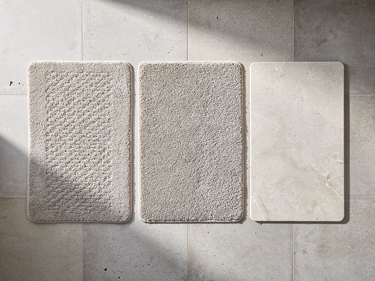 Several bath mats of different materials arranged side by side on a bathroom floor