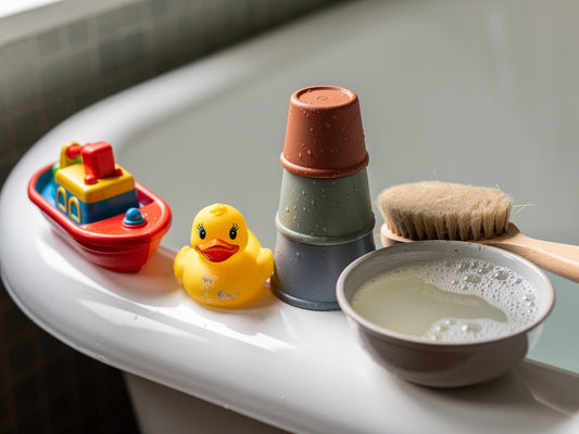 Colorful rubber duck and bath toys lined up on the edge of a tub next to a scrub brush and soapy water.
