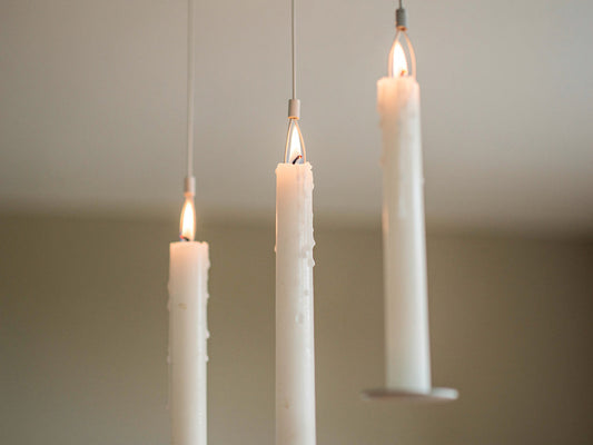 Three taper candles hanging at staggered heights, appearing to float.