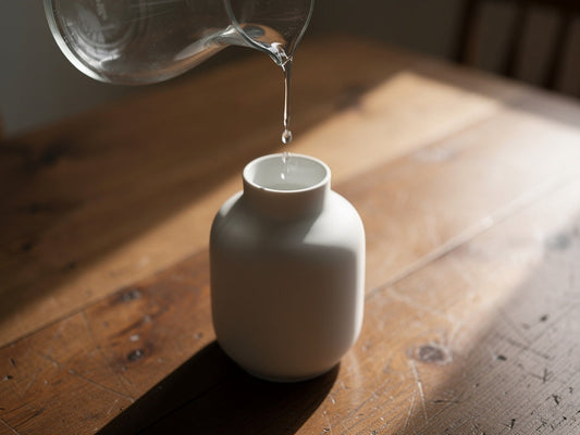 Water being poured into a white ceramic vase to test whether it holds water without leaking.