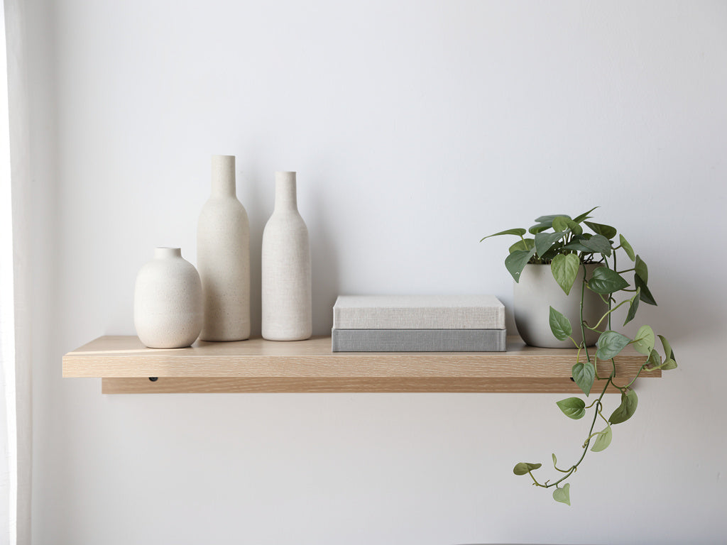 A floating shelf styled with three vases of different heights, a stack of books, and a small trailing plant, arranged with open space between objects