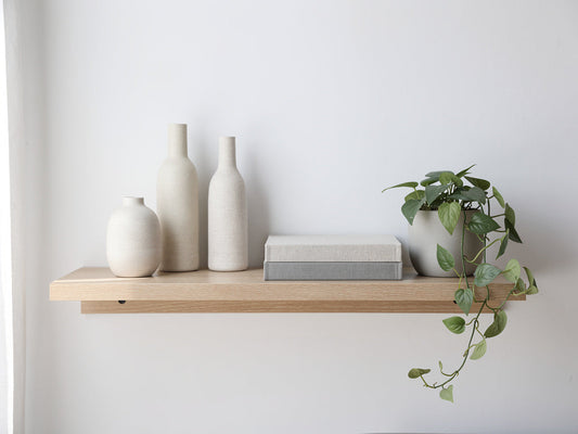 A floating shelf styled with three vases of different heights, a stack of books, and a small trailing plant, arranged with open space between objects