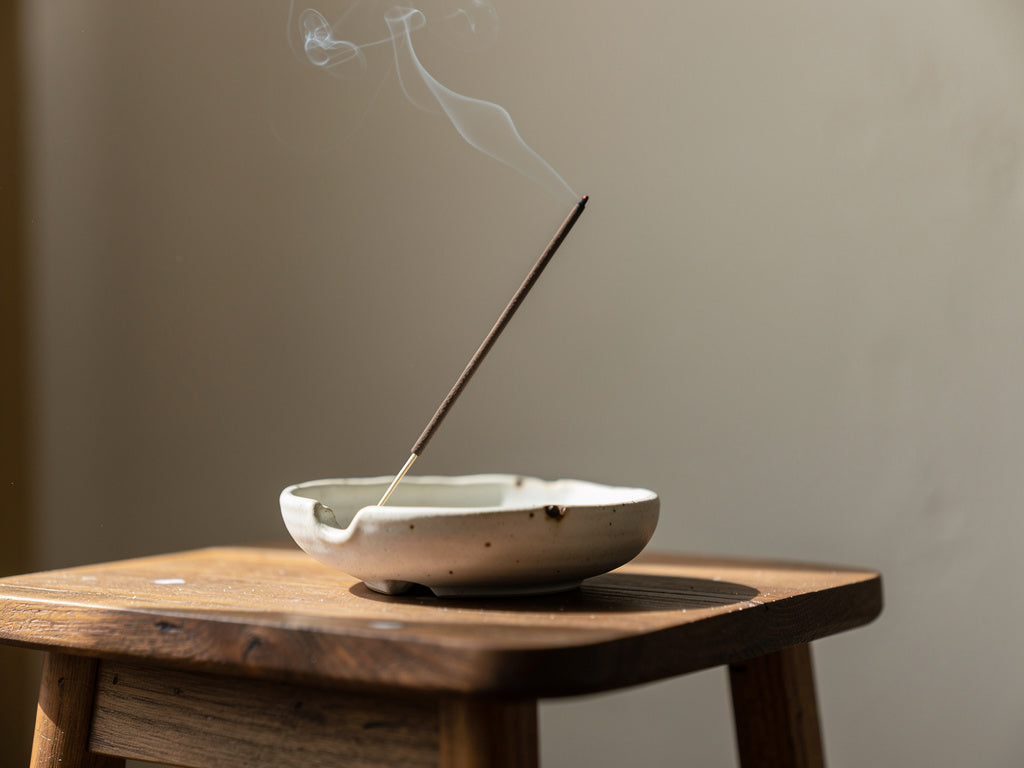 A lit incense stick sending up a thin curl of smoke from a ceramic holder