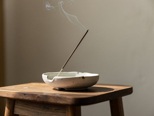 A lit incense stick sending up a thin curl of smoke from a ceramic holder
