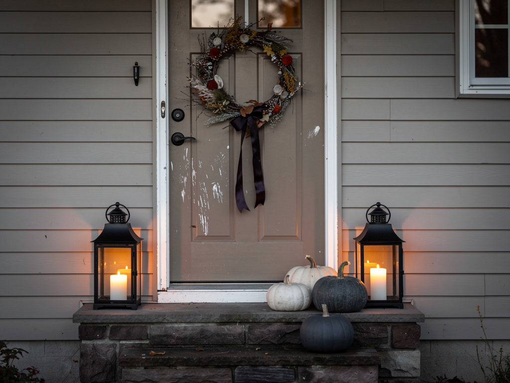 A house's front entry styled for Halloween with a dried floral wreath, black lanterns, and graduated matte pumpkins.