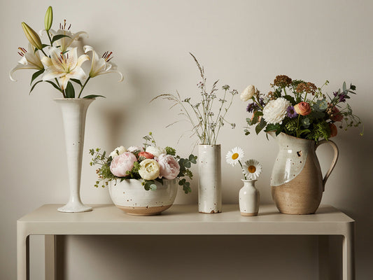 Five differently shaped vases in a row, each holding a flower suited to its own shape.