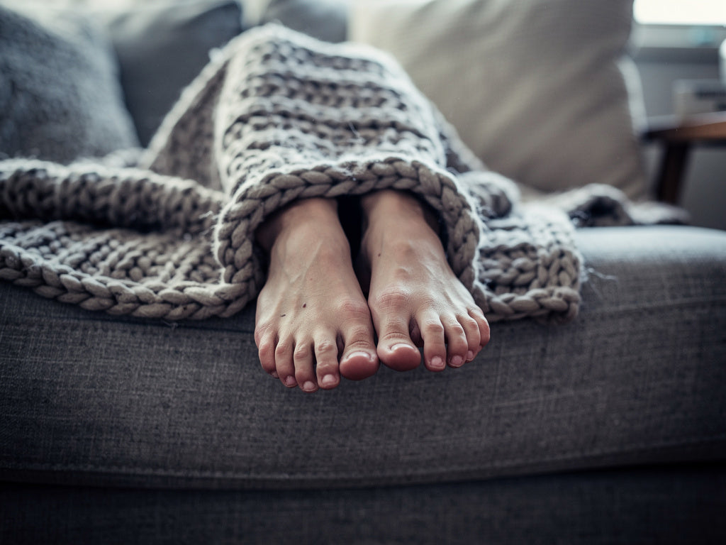 Bare feet peeking out from under a blanket on a couch